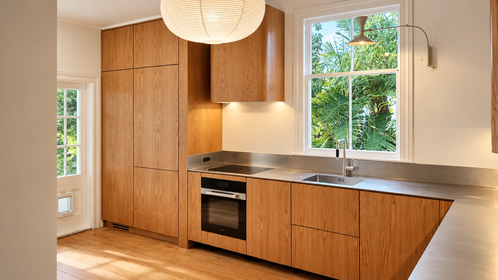 Grey Lynn oak kitchen sink wall — 5mm orbital satin-finish stainless steel benchtop with negative detail, integrated cooktop and garden outlook