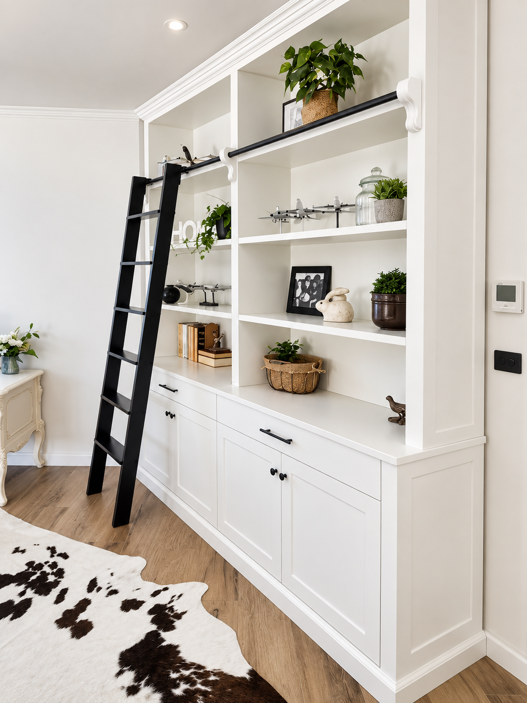 White built-in library bookcase with open shelving, cabinet base and black roller ladder