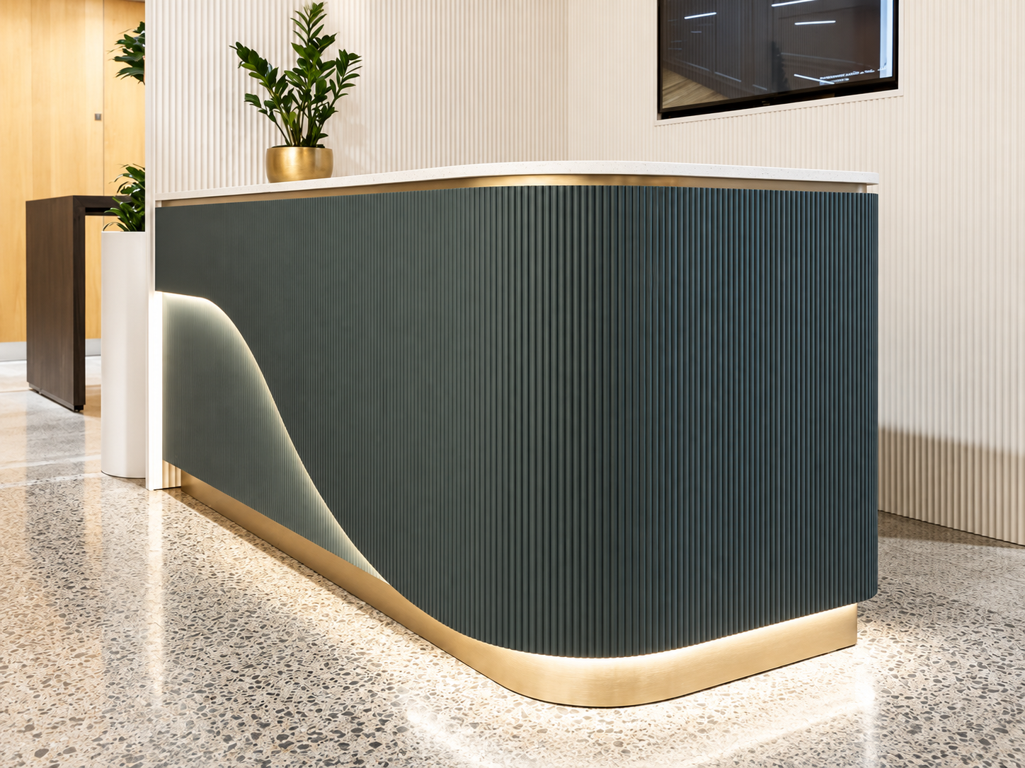 Dark green fluted joinery counter with curved brass base lighting and stone top