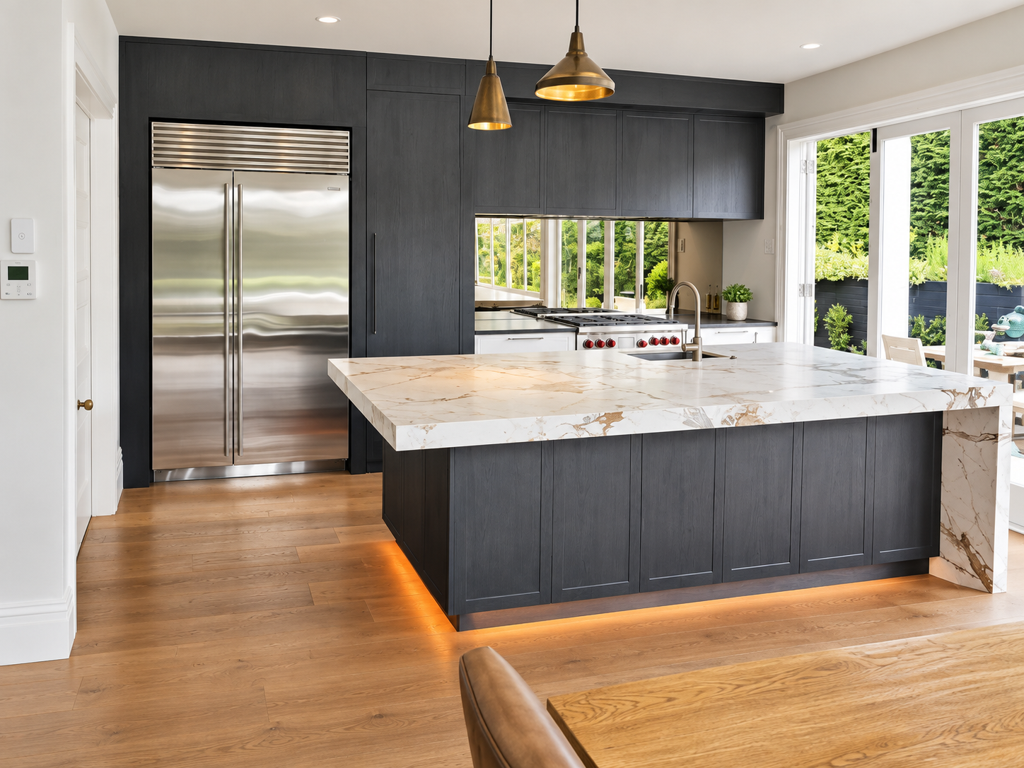Dark charcoal flat-panel kitchen with oversized waterfall marble island and brass pendants