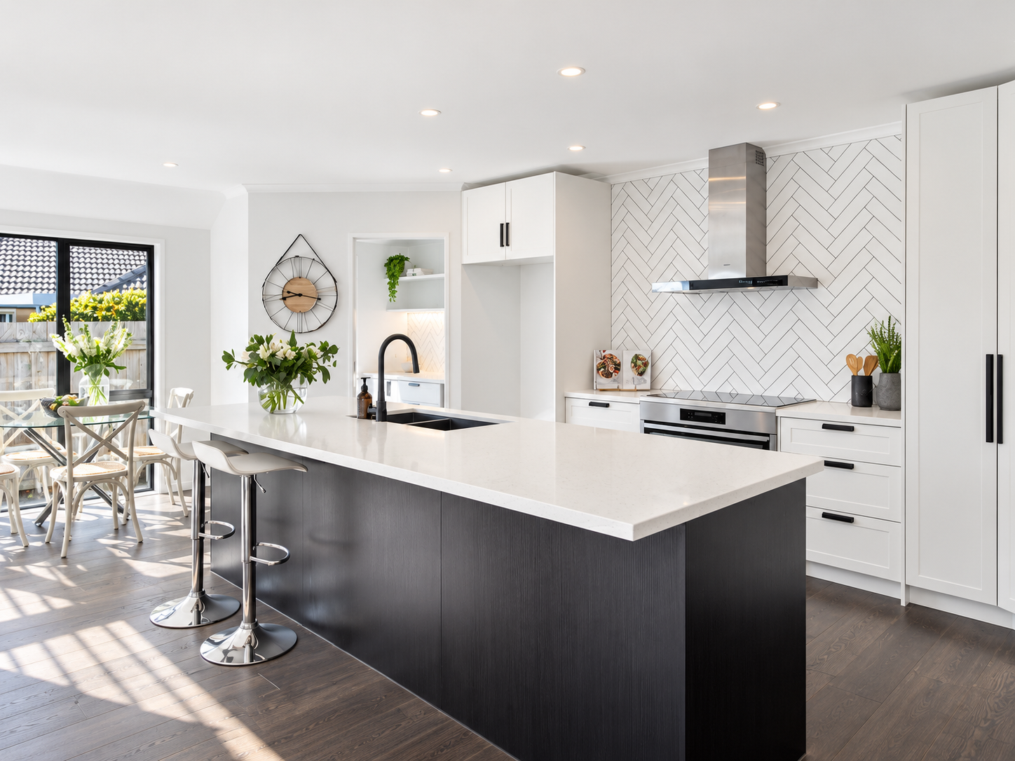 White flat-panel kitchen with dark textured island, white stone benchtop and herringbone tile splashback
